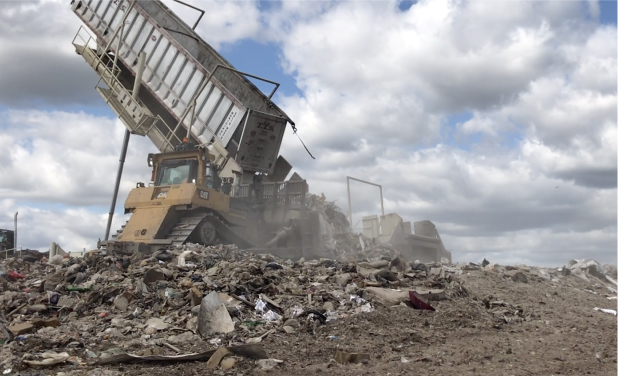 An image of a truck dumping garbage into a landfill pile. The sky is blue and filled with billowy clouds.