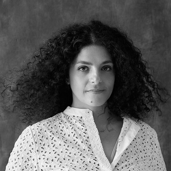 A black and white image of a Lebanese woman with dark curly hair wearing a white embroidered top.