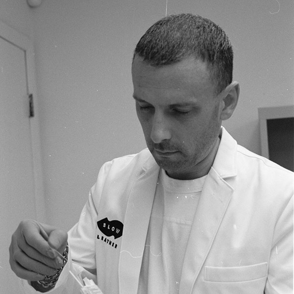 A black and white image of a person with short hair, with his hand on his chin, wearing a dark suit.