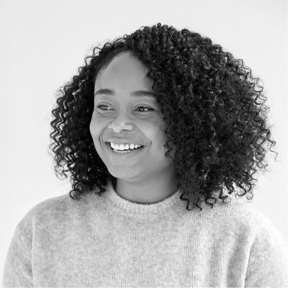 Kima Cooper, A black and white image of a smiling Nigerian woman with curly dark hair, wearing a light sweater.